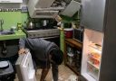 Muž v kuchyni neskoro v noci robí neporiadok a rozlieva jedlo pri otvorenej chladničke.