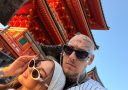 Pár v slnečných okuliaroch pózuje pred tradičnou japonskou architektúrou, živé farby chrámu a jasná obloha.